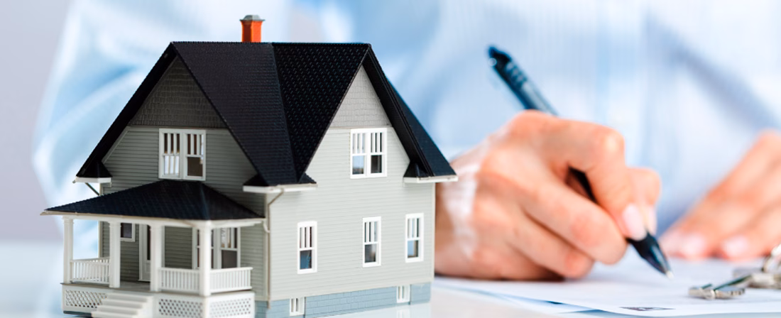 Miniatura de casa sobre mesa y persona firmando documento
