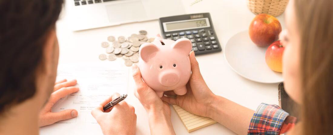 Dos personas calculando un presupuesto familiar con una hucha en forma de cerdo en las manos