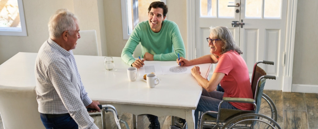 tres personas sentadas en una mesa, una de ellas en silla de ruedas 